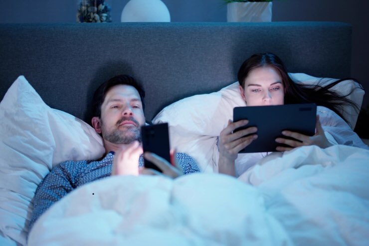 uomo con smartphone e donna con tablet nel letto